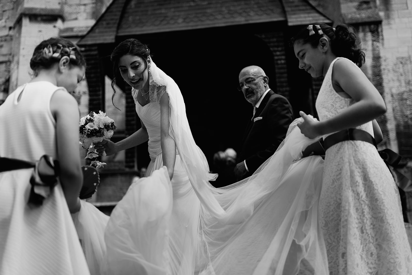 Mariage au Manoir de Corny en Normandie. Les demoiselles d'honneur remettent correctement la robe de la mariée